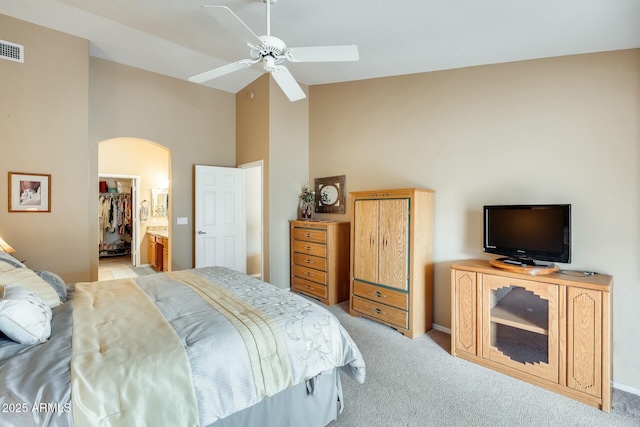 bedroom with arched walkways, high vaulted ceiling, ceiling fan, light colored carpet, and a walk in closet