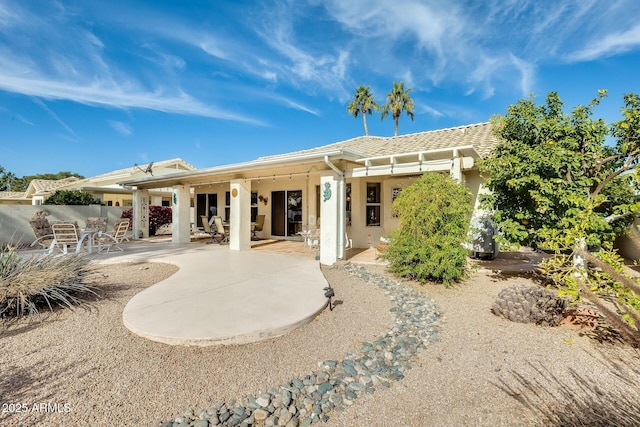 rear view of house with a patio area, a tile roof, fence, and stucco siding