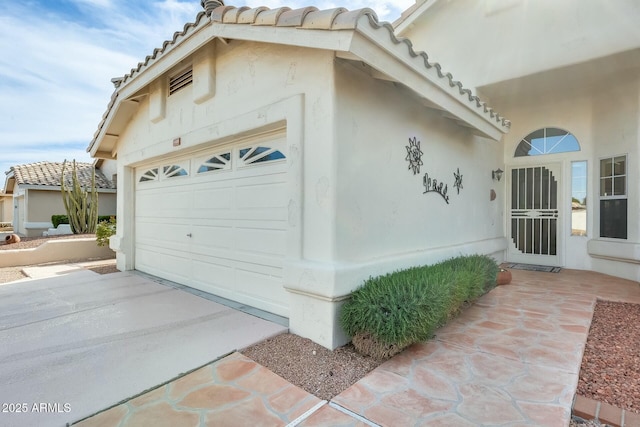 view of property exterior featuring an attached garage, stucco siding, driveway, and a tiled roof