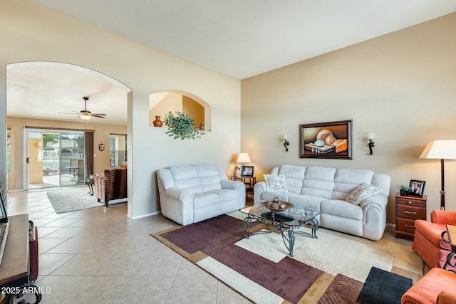 living room with arched walkways, light tile patterned flooring, ceiling fan, and baseboards