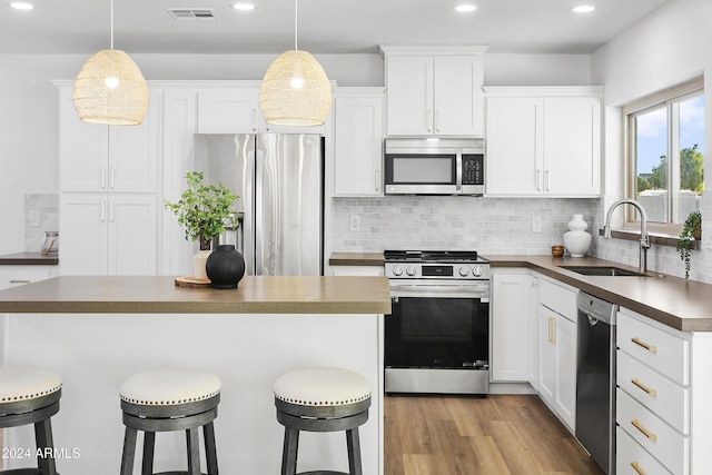 kitchen with decorative light fixtures, stainless steel appliances, white cabinetry, and sink