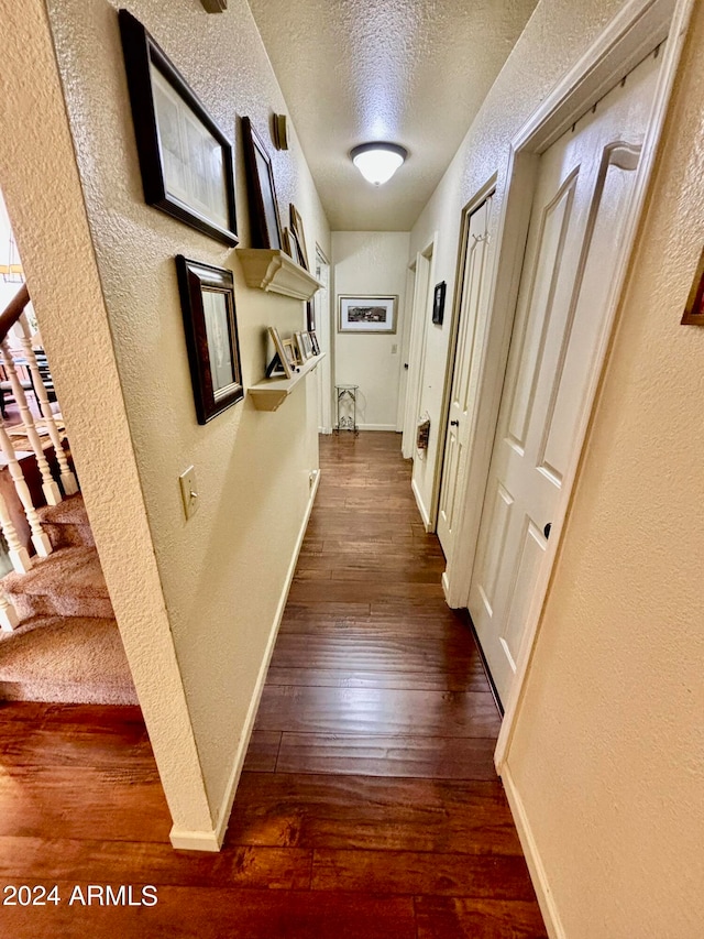 corridor with a textured ceiling and dark wood-type flooring