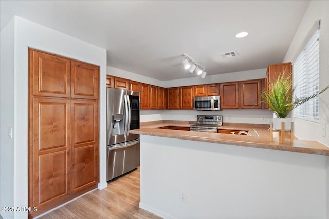 180 S 18th St, Coolidge, AZ 85128 - kitchen with stainless steel appliances, brown cabinets, a peninsula, light wood-type flooring, and light countertops