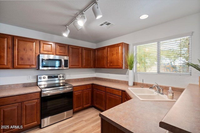 180 S 18th St, Coolidge, AZ 85128 - kitchen with appliances with stainless steel finishes, a sink, brown cabinetry, and light wood finished floors