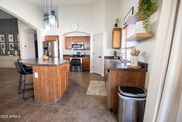 kitchen featuring arched walkways, stainless steel appliances, a sink, a center island, and dark countertops