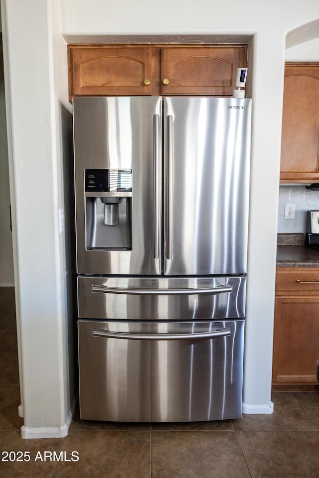 kitchen featuring dark countertops, dark tile patterned flooring, brown cabinetry, and stainless steel refrigerator with ice dispenser