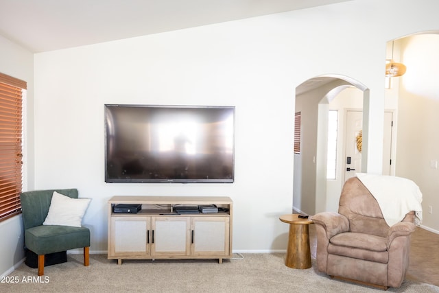 living area featuring baseboards, arched walkways, and light colored carpet