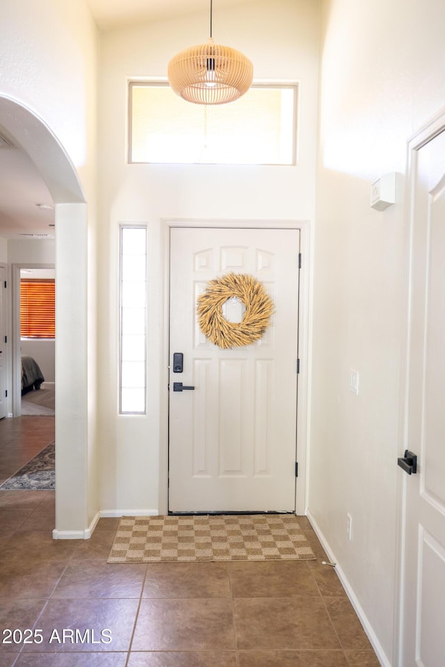 foyer entrance with arched walkways, baseboards, and a high ceiling