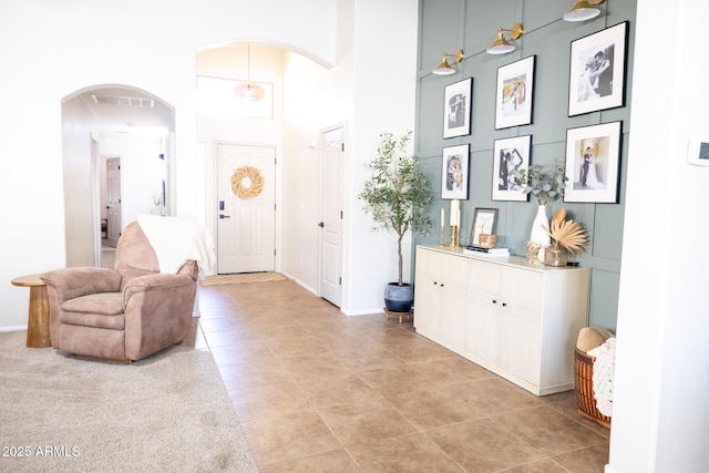 foyer entrance with visible vents, arched walkways, baseboards, a high ceiling, and light tile patterned flooring