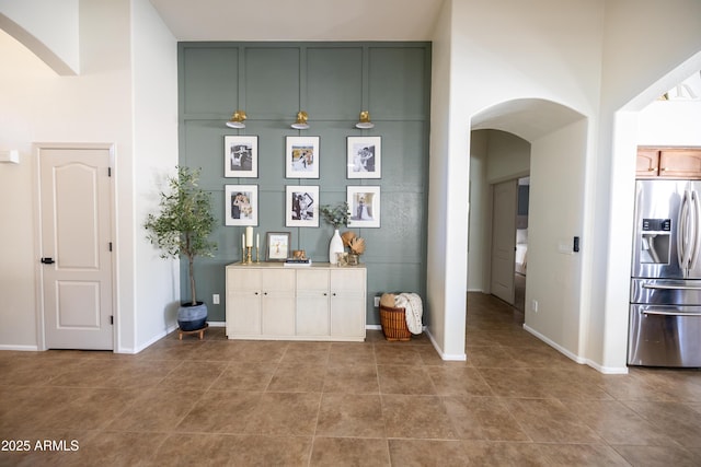 kitchen with stainless steel fridge, arched walkways, baseboards, ceiling fan, and a high ceiling