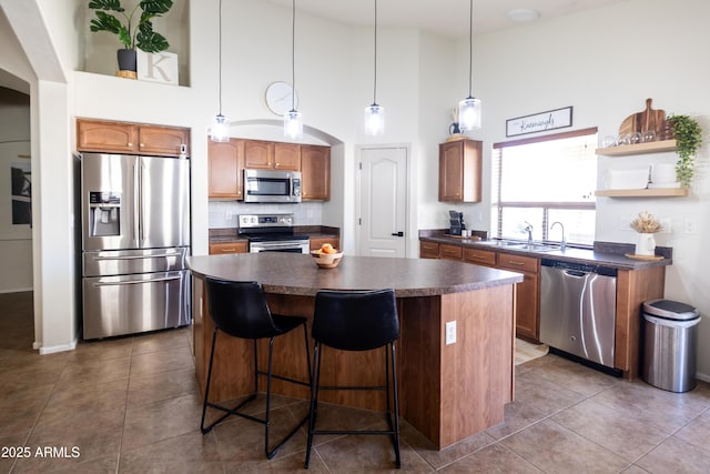 kitchen with decorative light fixtures, stainless steel appliances, dark countertops, a kitchen island, and tile patterned floors