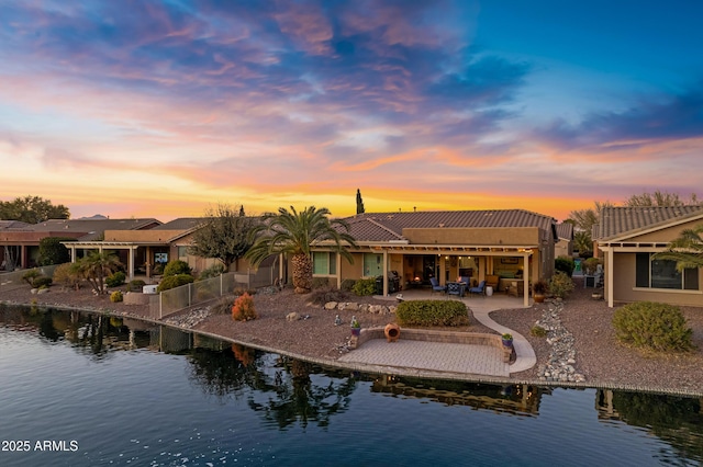 back house at dusk with a water view and a patio