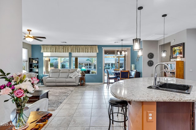 kitchen with ceiling fan, sink, hanging light fixtures, light stone counters, and light tile patterned floors