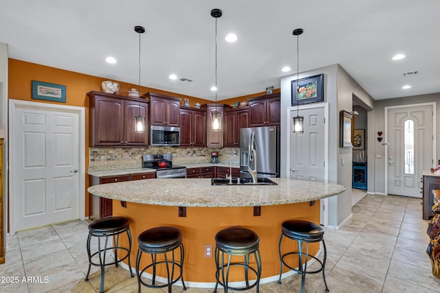 kitchen featuring stainless steel appliances, an island with sink, a kitchen breakfast bar, backsplash, and sink