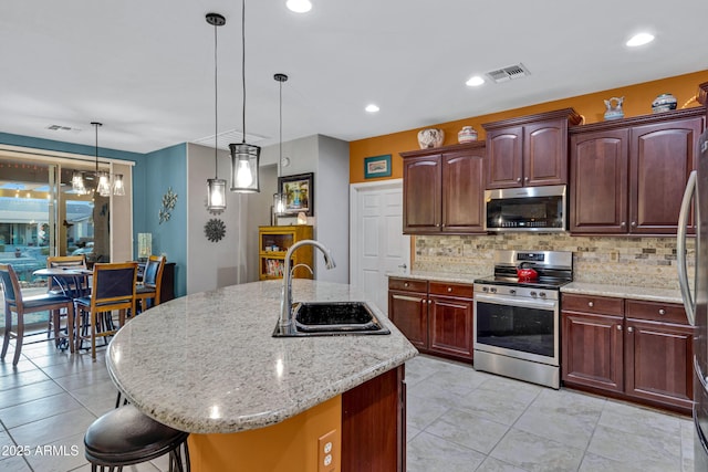 kitchen with stainless steel appliances, a kitchen island with sink, hanging light fixtures, and sink