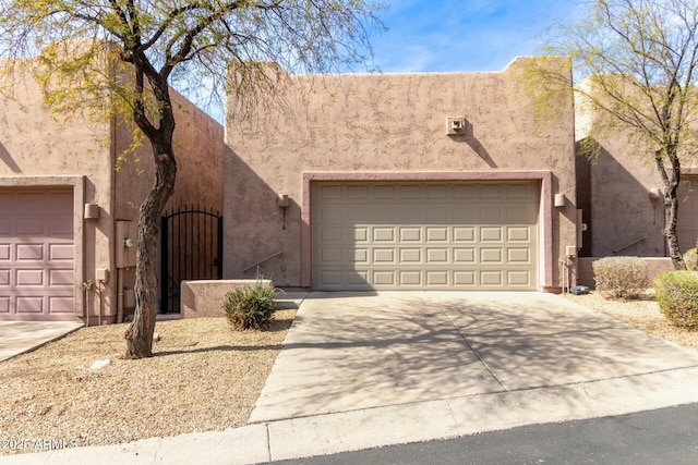 pueblo-style home with a garage, a gate, concrete driveway, and stucco siding