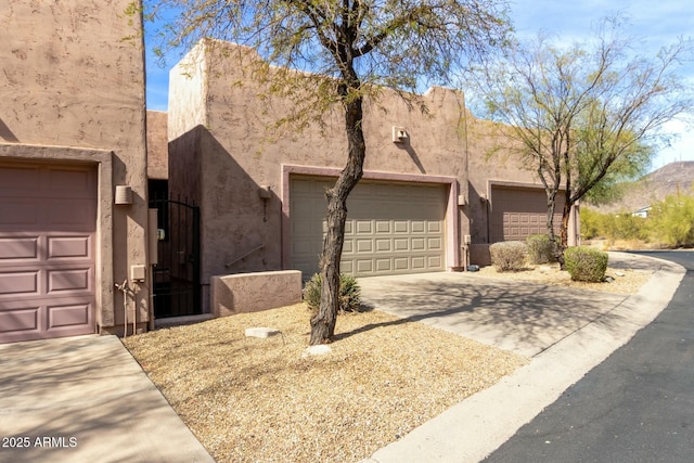 pueblo-style home featuring driveway, an attached garage, and stucco siding