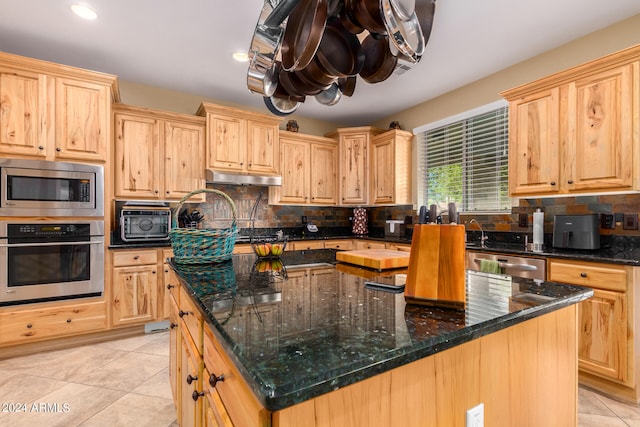 kitchen with light brown cabinets, light tile patterned floors, a kitchen island, appliances with stainless steel finishes, and dark stone counters