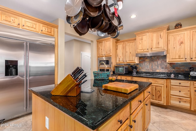 kitchen with dark stone counters, built in appliances, tasteful backsplash, a center island with sink, and light brown cabinets