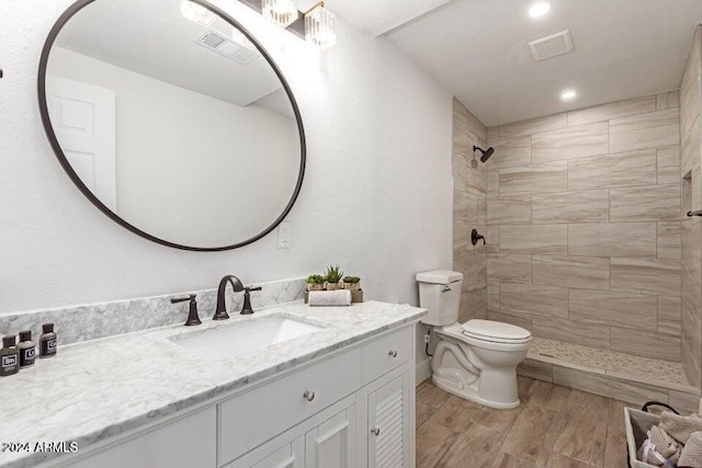 bathroom with vanity, toilet, wood-type flooring, and tiled shower