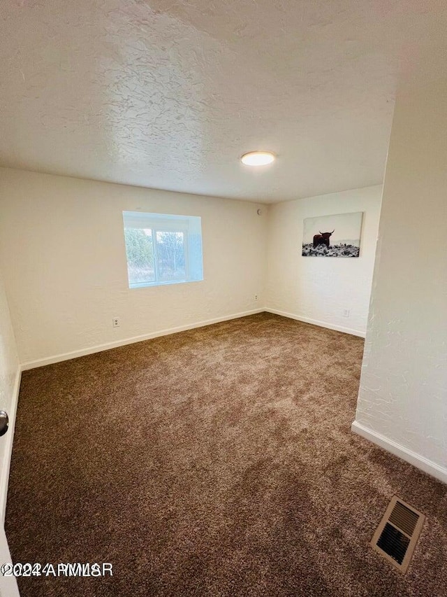 unfurnished room featuring a textured ceiling and dark colored carpet