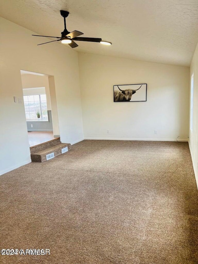 empty room featuring a textured ceiling, ceiling fan, vaulted ceiling, and carpet