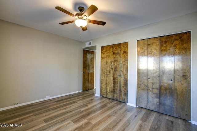 unfurnished bedroom featuring ceiling fan, two closets, and hardwood / wood-style floors