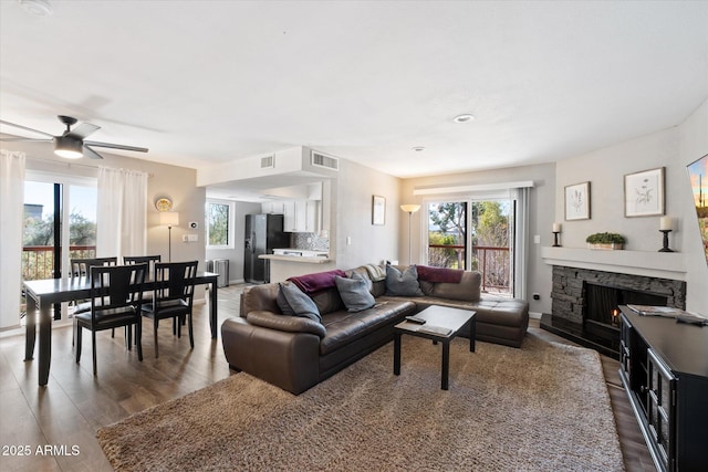 living room with dark hardwood / wood-style flooring, a stone fireplace, and a wealth of natural light