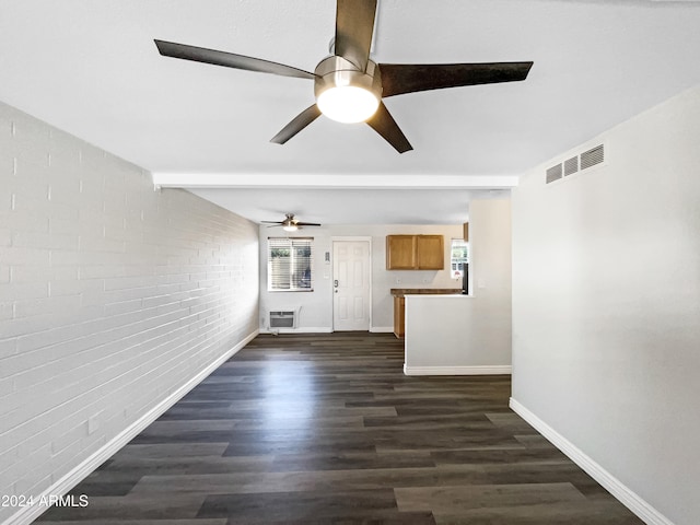 unfurnished living room featuring ceiling fan, a healthy amount of sunlight, brick wall, and dark hardwood / wood-style flooring