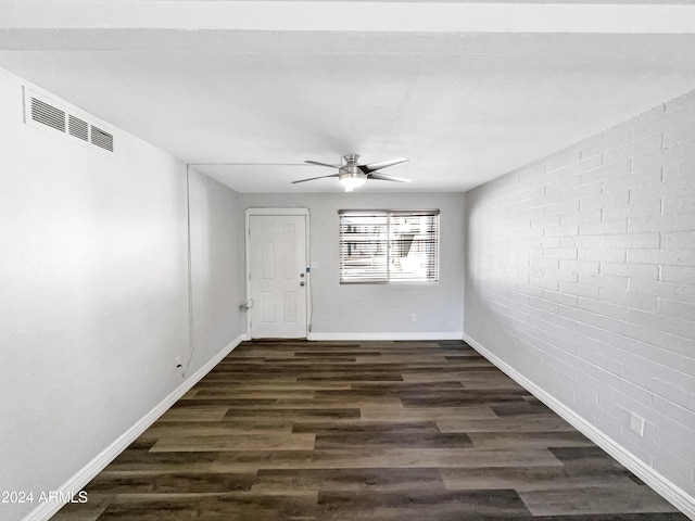 spare room featuring dark wood-type flooring, ceiling fan, and brick wall