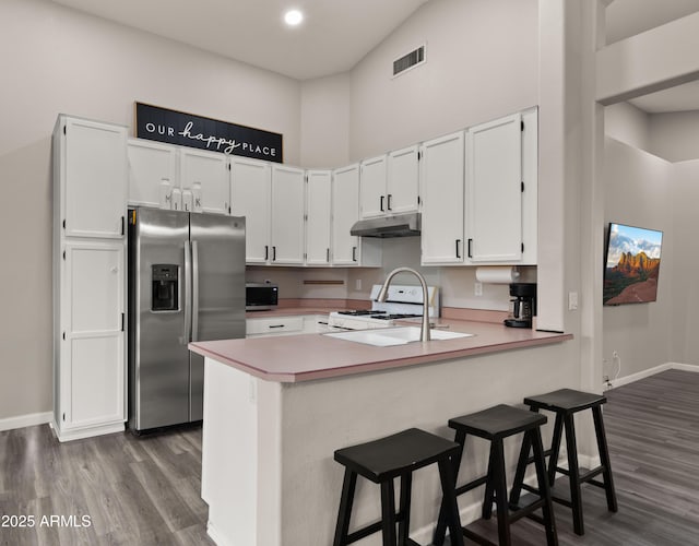 kitchen featuring kitchen peninsula, stainless steel appliances, a kitchen breakfast bar, dark wood-type flooring, and white cabinets