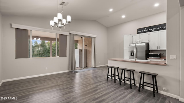 kitchen with white cabinetry, stainless steel fridge, a breakfast bar area, hanging light fixtures, and vaulted ceiling