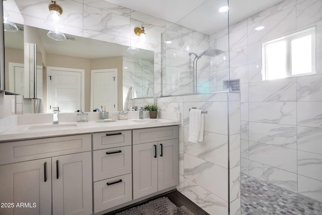 full bathroom featuring double vanity, walk in shower, a sink, and tile walls