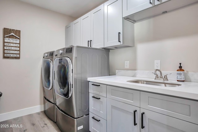 laundry area with light wood-style flooring, a sink, baseboards, cabinet space, and washing machine and clothes dryer