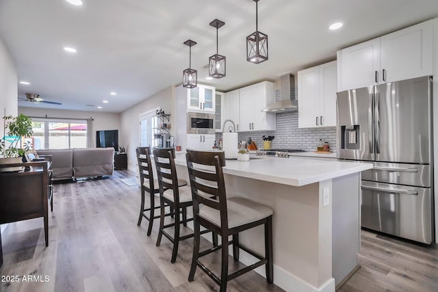 kitchen featuring stainless steel appliances, tasteful backsplash, light wood-style flooring, wall chimney range hood, and a kitchen bar