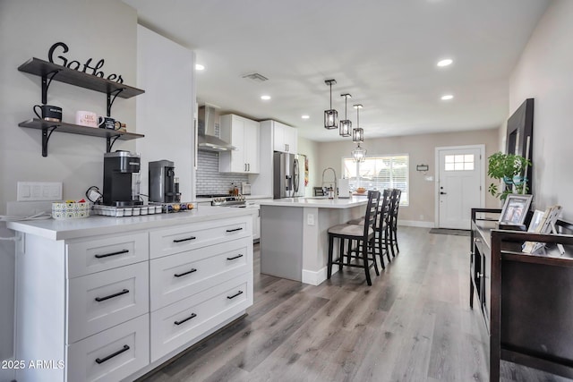 kitchen with light countertops, stainless steel refrigerator with ice dispenser, a kitchen breakfast bar, and wall chimney range hood
