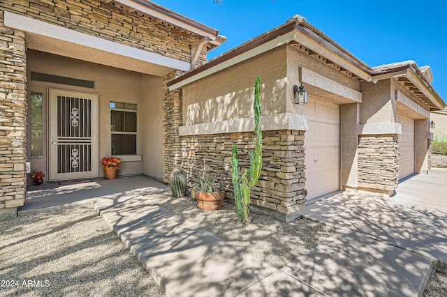 doorway to property with a garage, stone siding, and stucco siding