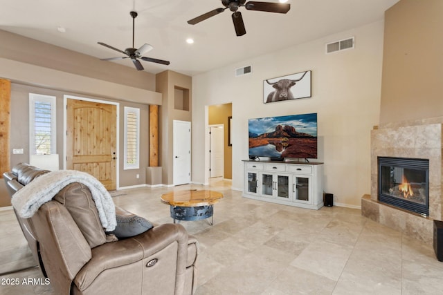 living area featuring visible vents, baseboards, ceiling fan, and a tile fireplace