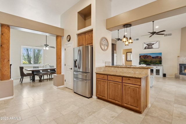 kitchen featuring visible vents, brown cabinets, stainless steel fridge with ice dispenser, a towering ceiling, and open floor plan