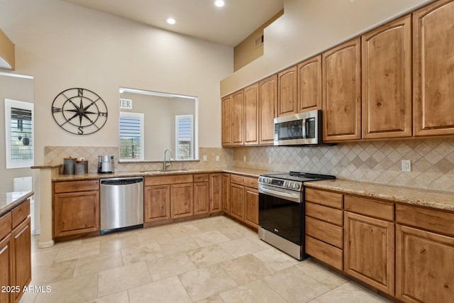 kitchen featuring light stone counters, brown cabinetry, a sink, appliances with stainless steel finishes, and backsplash