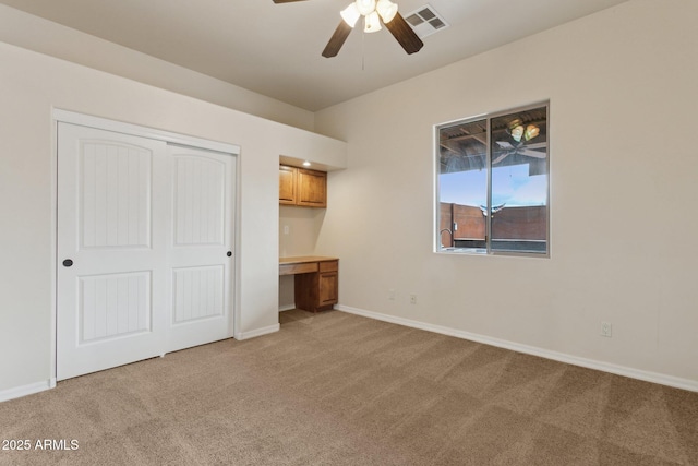 unfurnished bedroom with baseboards, visible vents, built in study area, a closet, and light carpet