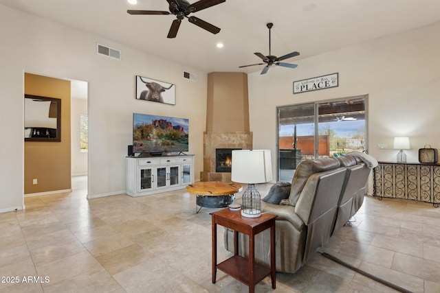 living room featuring visible vents, a large fireplace, baseboards, and a towering ceiling