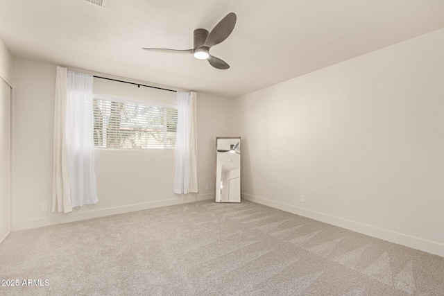 empty room featuring light colored carpet, a ceiling fan, and baseboards