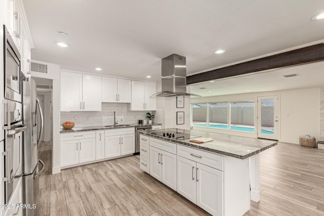 kitchen with island range hood, a center island, dark stone counters, a sink, and appliances with stainless steel finishes