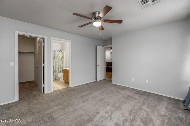 unfurnished bedroom featuring a walk in closet, light colored carpet, ceiling fan, ensuite bath, and a closet