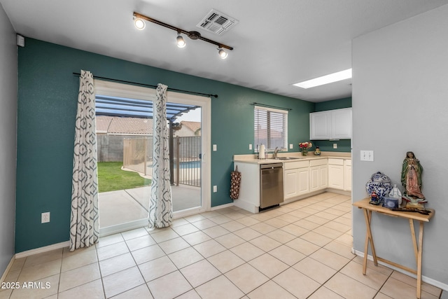 kitchen with sink, dishwasher, a skylight, white cabinets, and light tile patterned flooring