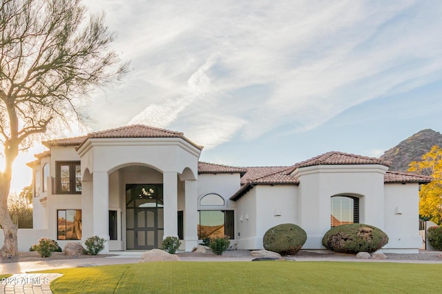 mediterranean / spanish-style house featuring a front yard, a tile roof, and stucco siding