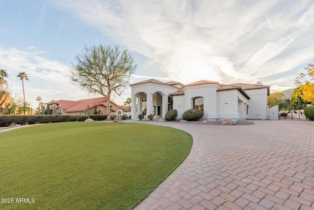 mediterranean / spanish-style home featuring stucco siding, a tile roof, decorative driveway, and a front yard