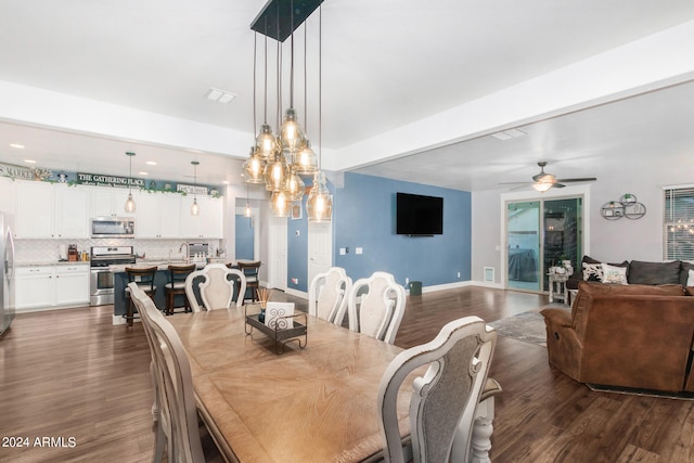 dining room with dark wood-type flooring, ceiling fan with notable chandelier, and beamed ceiling