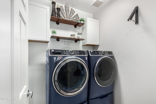 clothes washing area featuring washing machine and dryer, visible vents, and cabinet space